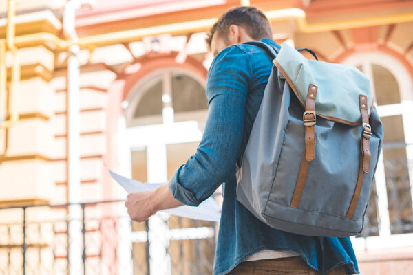 rear view of young tourist with backpack looking at map on street
