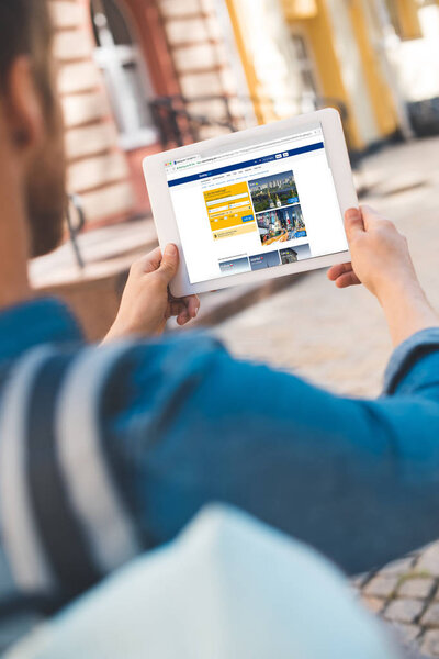 cropped shot of young man using tablet with booking website on screen while walking by street
