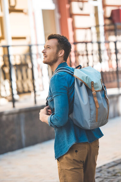handsome young tourist with backpack walking by street and looking up