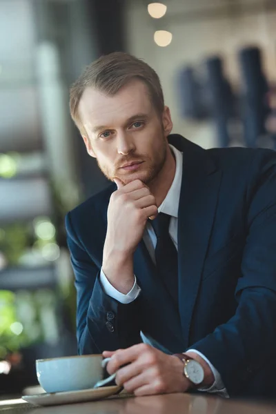 portrait of stylish businessman in suit with cup of coffee having coffee break in cafe