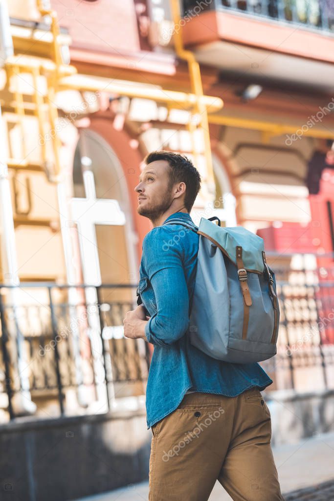attractive young tourist with backpack walking by street and looking up