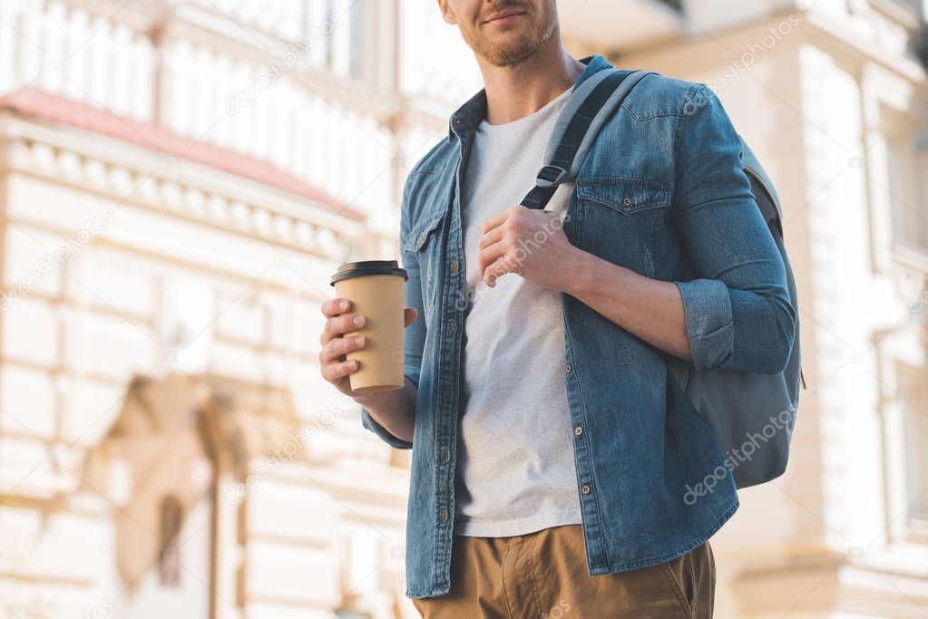 cropped shot of young man with coffee to go and backpack walking on street