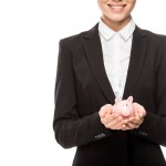 Cropped shot of smiling young businesswoman holding piggy bank isolated on white