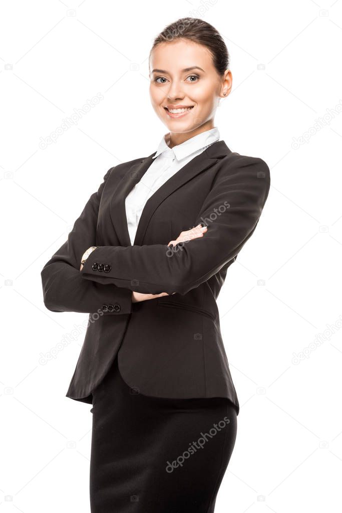 happy young businesswoman in suit looking at camera with crossed arms isolated on white