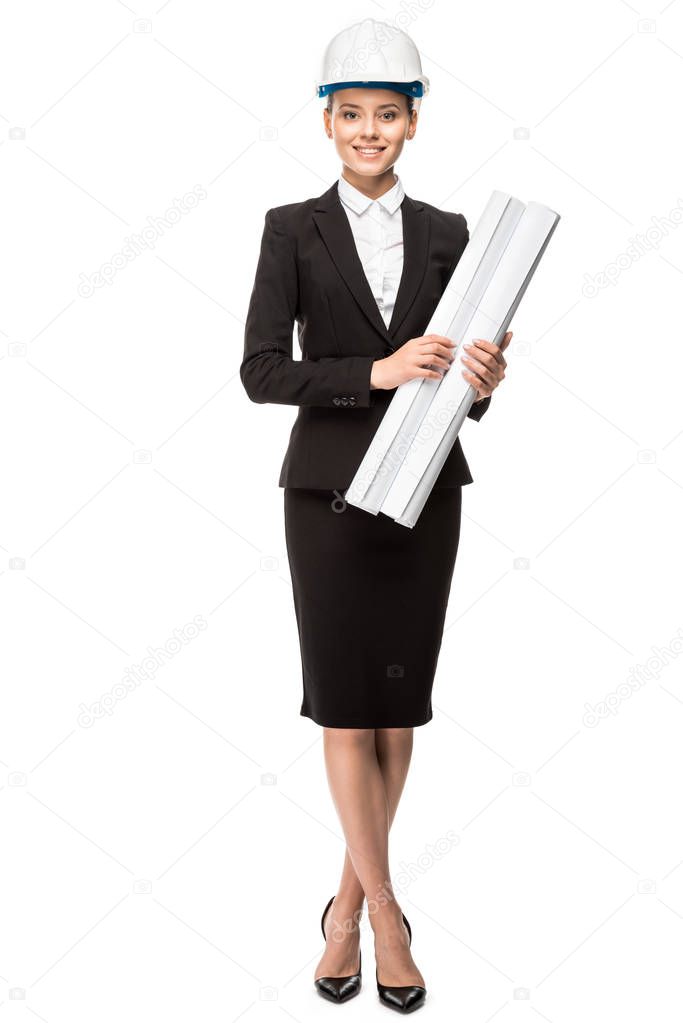 attractive young female architect in helmet and suit holding blueprints and looking at camera isolated on white