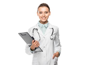 cheerful young female doctor in medical coat holding clipboard isolated on white clipart