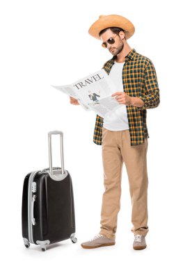 stylish male tourist in sunglasses reading travel newspaper near wheeled bag isolated on white  clipart