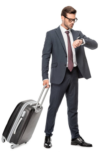 handsome young businessman with luggage looking at wrist watch isolated on white