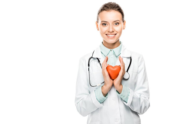 cheerful young female doctor with stethoscope over neck showing heart symbol isolated on white