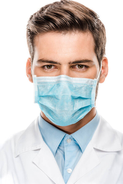 serious young male doctor in medical mask looking at camera isolated on white 