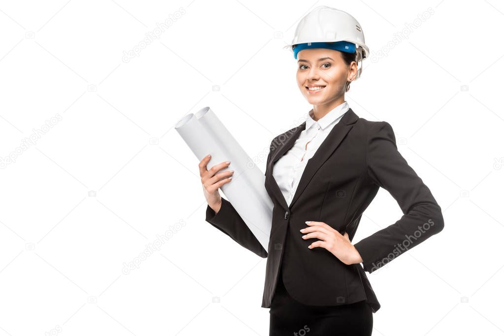 beautiful young female architect in helmet and suit holding blueprints and looking at camera isolated on white