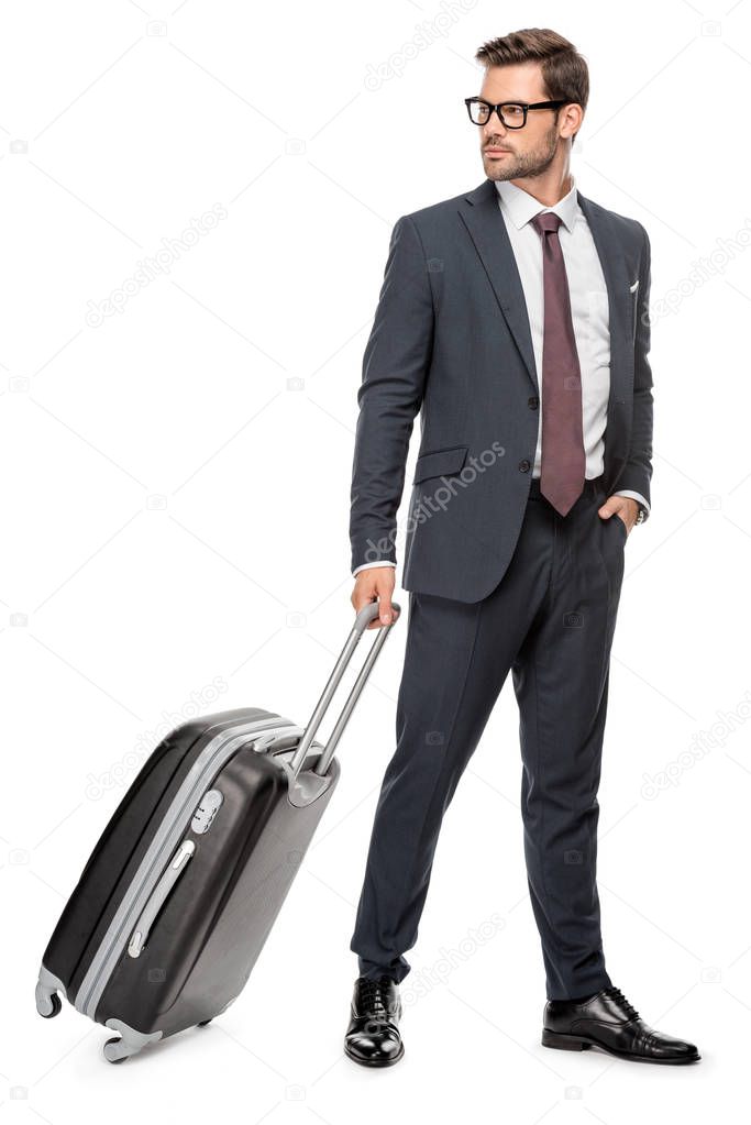 handsome young businessman walking with luggage and looking away isolated on white