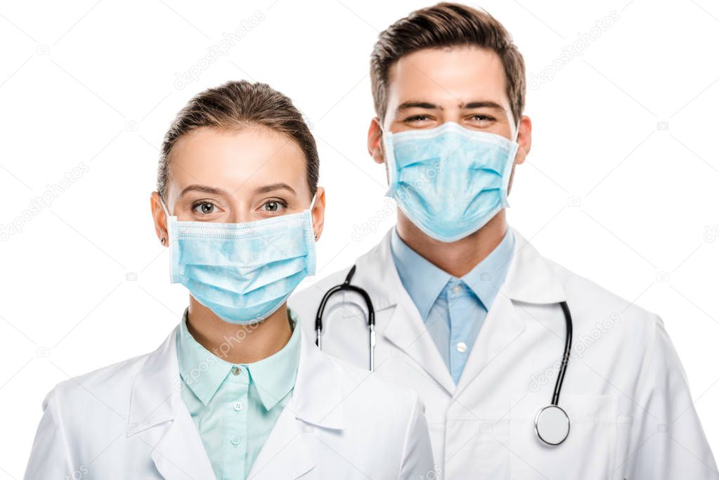 portrait of happy young doctors in medical masks looking at camera isolated on white