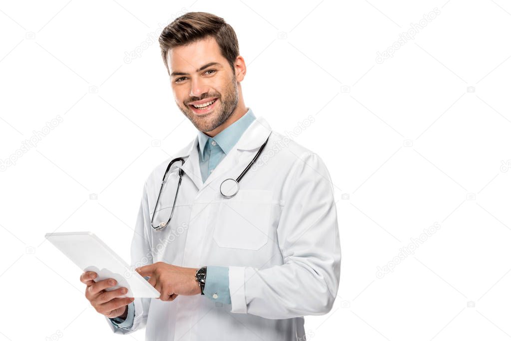 smiling young male doctor in medical coat using digital tablet isolated on white 