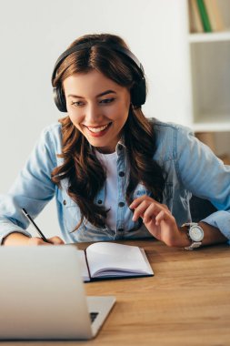 portrait of young smiling woman in headphones taking part in webinar in office clipart