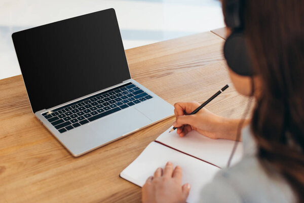 partial view of businesswoman in headphones with notebook taking part in webinar in office