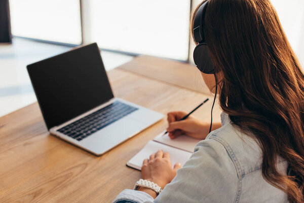 partial view of businesswoman in headphones with notebook taking part in webinar in office