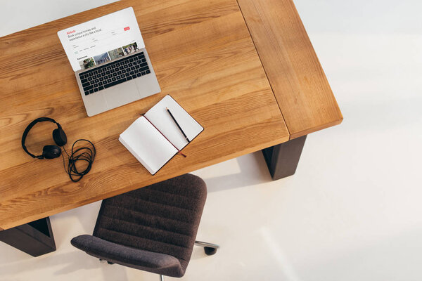 top view of laptop with airbnb website, headphones and notebook on wooden table with office chair near by