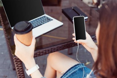 Tablo boş ekran ile Smartphone kullanarak ve tek kullanımlık kahve fincanı tutan kadın