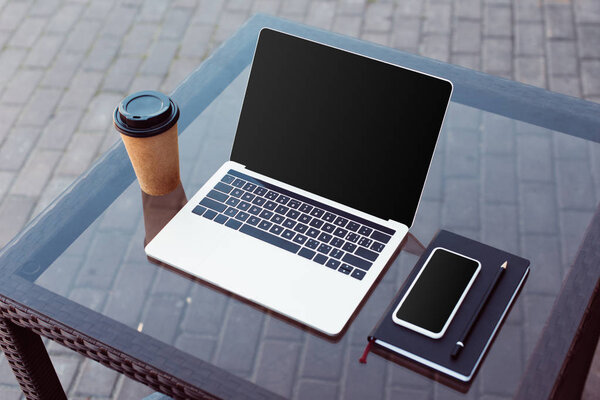 smartphone and laptop with blank screens on table at street cafe