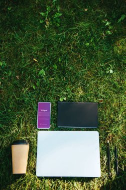 smartphone instagram cihazı, laptop ve kağıt bardak kahve ile üstten görünüm Park yeşil çimenlerin üzerinde