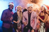 excited multiethnic friends in santa hats celebrating new year with champagne glasses on party