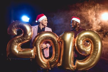 Noel Baba şapkaları birbirine 2019 yeni yıl duman ve arkadan aydınlatmalı altın balonları tutarken bakarak çok kültürlü arkadaşlar 