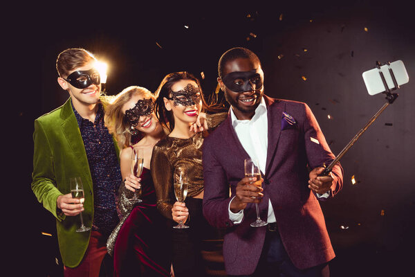 happy multiethnic luxury couples in carnival masks taking selfie on smartphone