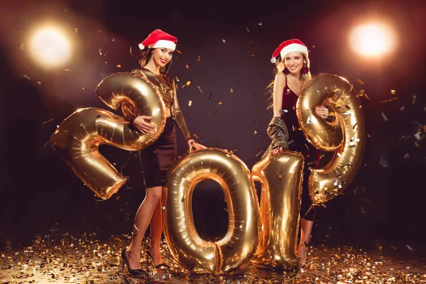 漂亮的女孩在圣诞老人的帽子摆在金色的五彩纸屑2019新年气球 — 图库照片