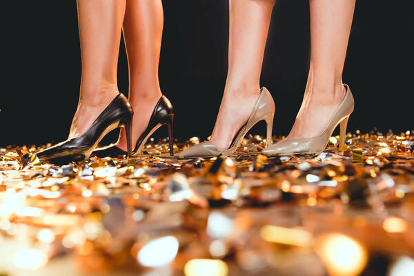 cropped view of girls in high heels standing on golden confetti on party