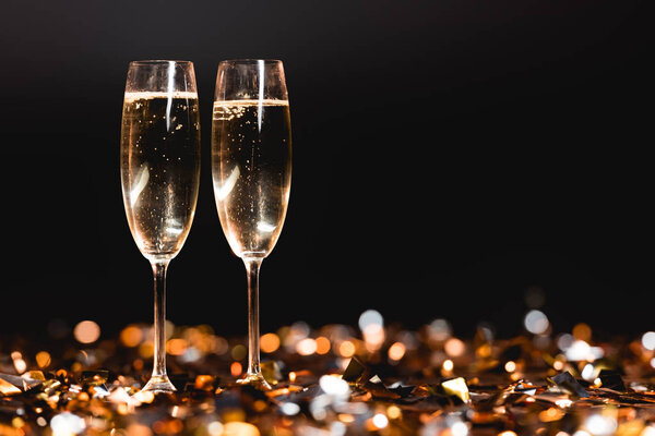 champagne glasses on golden confetti on black for new year celebration