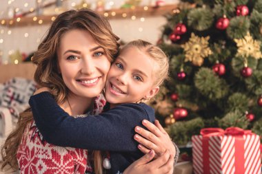 Anne ve kızı sarılma ve kamera Noel ağacı evde yakınındaki bakarak gülen