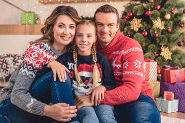 Anne ve kızı sarılma ve Noel ağacı ve evde hediye yakınında oturan gülümseyen