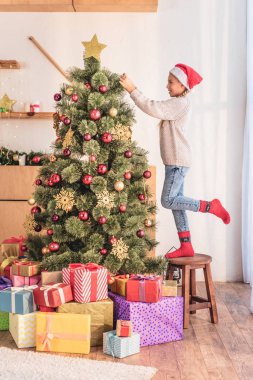 taburede duran ve hediye kutuları ile Noel ağacı süsleme santa şapka içinde mutlu çocuk