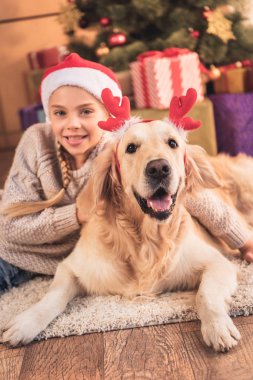 Noel Baba şapkası ve golden retriever köpek Noel yalan geyik boynuzları ile gülümseyen çocuk sunar