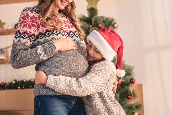 Обрезанное Изображение Дочери Шляпе Санты Обнимающей Беременную Мать Возле Рождественской — стоковое фото