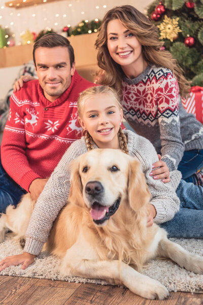 счастливые родители и дочь с золотистой собакой ретривер возле рождественской елки

