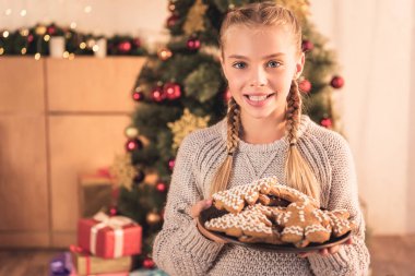 plaka ile geleneksel gingerbread çerezleri evde Noel ağacı ile tutarak gülümseyen kadın çocuk
