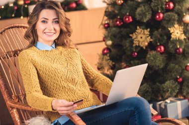 gülümseyen kadın ile kredi kartı ve dizüstü evde Noel ağacı ile online alışveriş