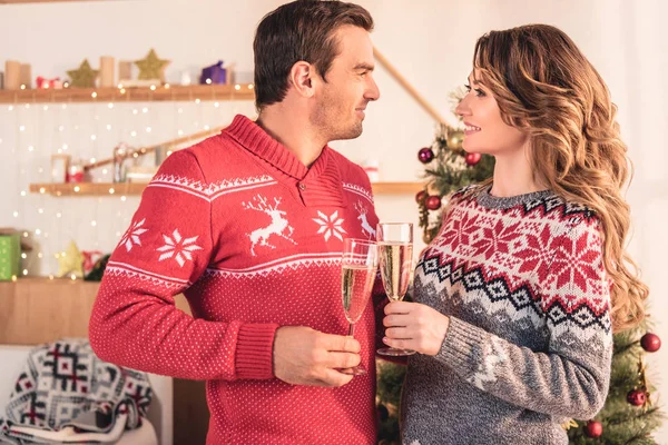 Smiling Couple Christmas Sweaters Holding Champagne Glasses Looking Each Other — Free Stock Photo