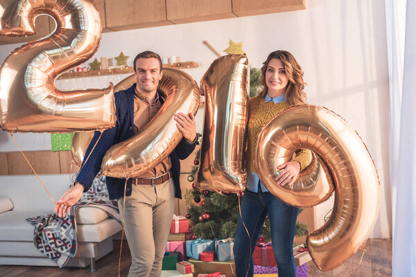 happy couple holding 2019 new year golden balloons at home with christmas tree and gift boxes
