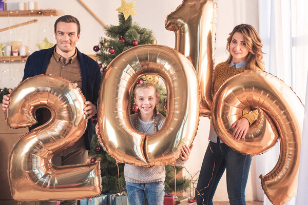 smiling family holding 2019 new year golden balloons at home with christmas tree