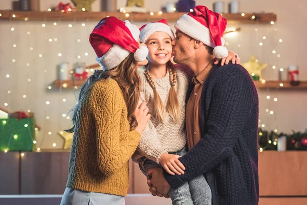 Šťastní Rodiče Santa Klobouky Líbání Usmívající Dceru Vánoce — Stock fotografie