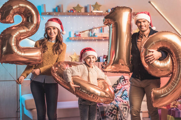 happy parents with daughter in santa hats holding 2019 new year golden balloons 