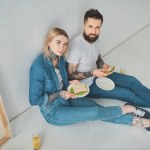 High angle view of happy young couple holding sandwiches and smiling at camera in new house