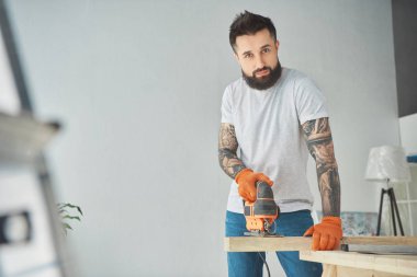 Elektrikli testere kullanarak ve kameraya bakarak yakışıklı sakallı dövmeli adam