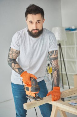 Elektrikli testere kullanarak ve kameraya bakarak sakallı yakışıklı