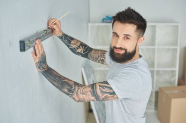 yakışıklı düzey aracı tutarak ve ev geliştirme sırasında kameraya gülümseyen genç adam sakallı