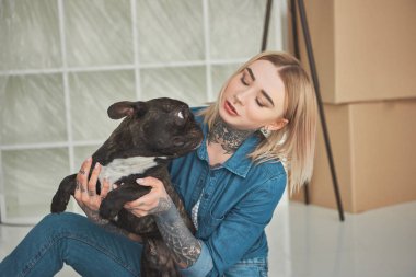 beautiful tattooed girl playing with french bulldog in new home clipart