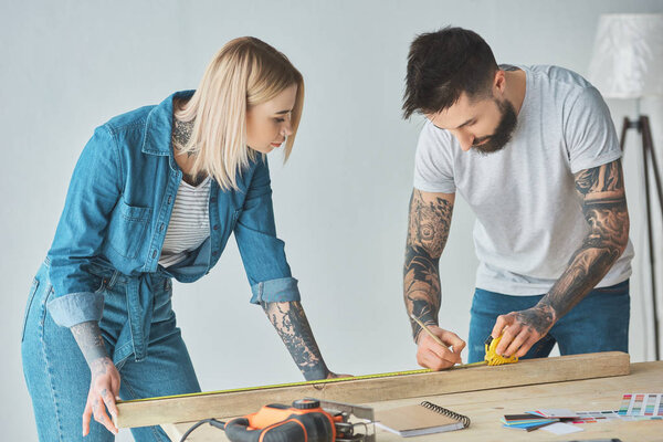 young tattooed couple working with pencil, wooden plank and measuring tape